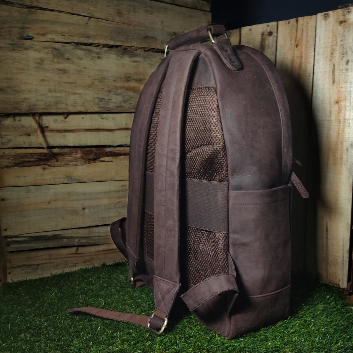 May include: A brown leather backpack with a mesh back panel and adjustable straps. The backpack has a zippered pocket on the front and a top handle.
