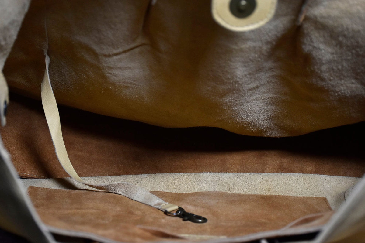 May include: A light-colored leather tote bag with a spacious interior. The bag features a beige interior lining, a strap, and a metal clasp. The leather has a textured appearance, and the bag appears to be open.