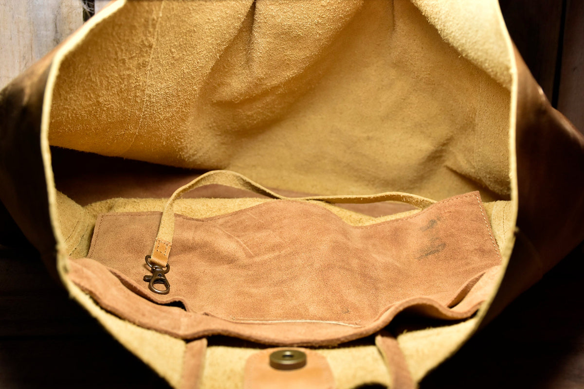 May include: A brown leather tote bag with a suede lining and a small leather strap with a metal clasp. The bag is open and the lining is visible.