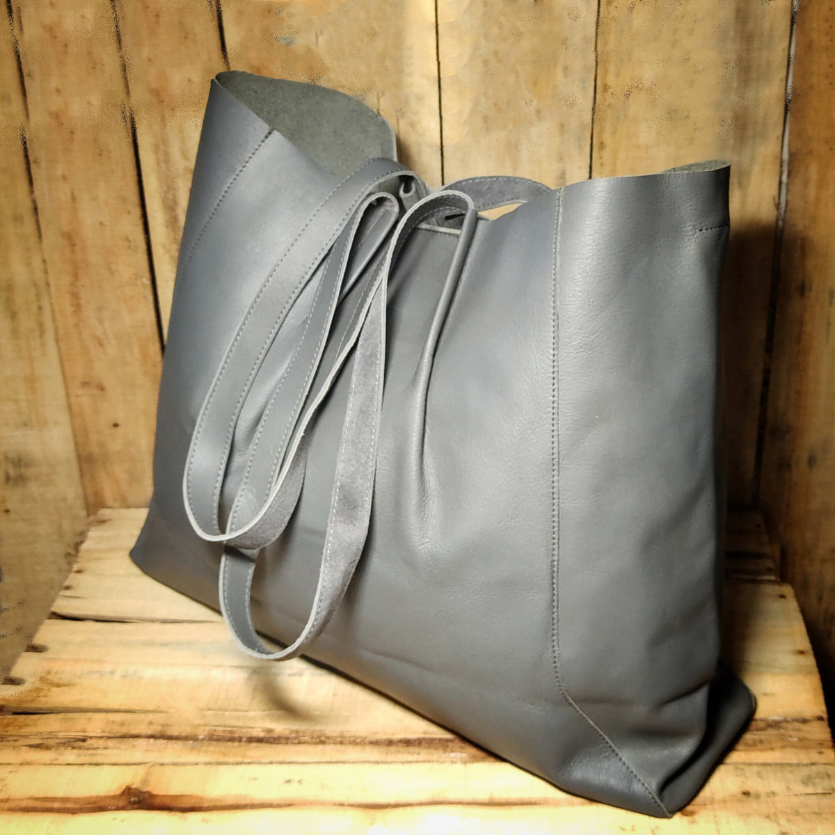 May include: A large gray leather tote bag with two long straps. The bag is made of a soft, supple leather and has a spacious interior.
