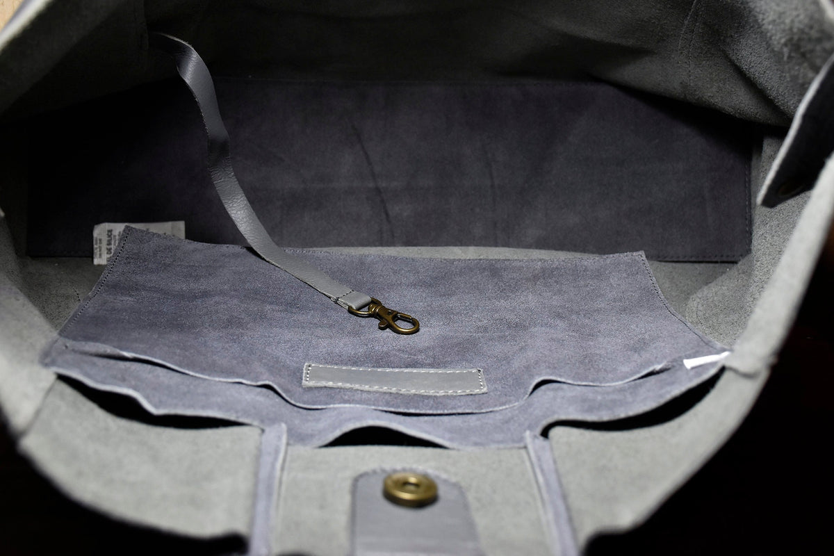May include: The inside of a gray tote bag with a gray suede lining. The bag has a small pocket on the inside and a metal hook attached to a strap.
