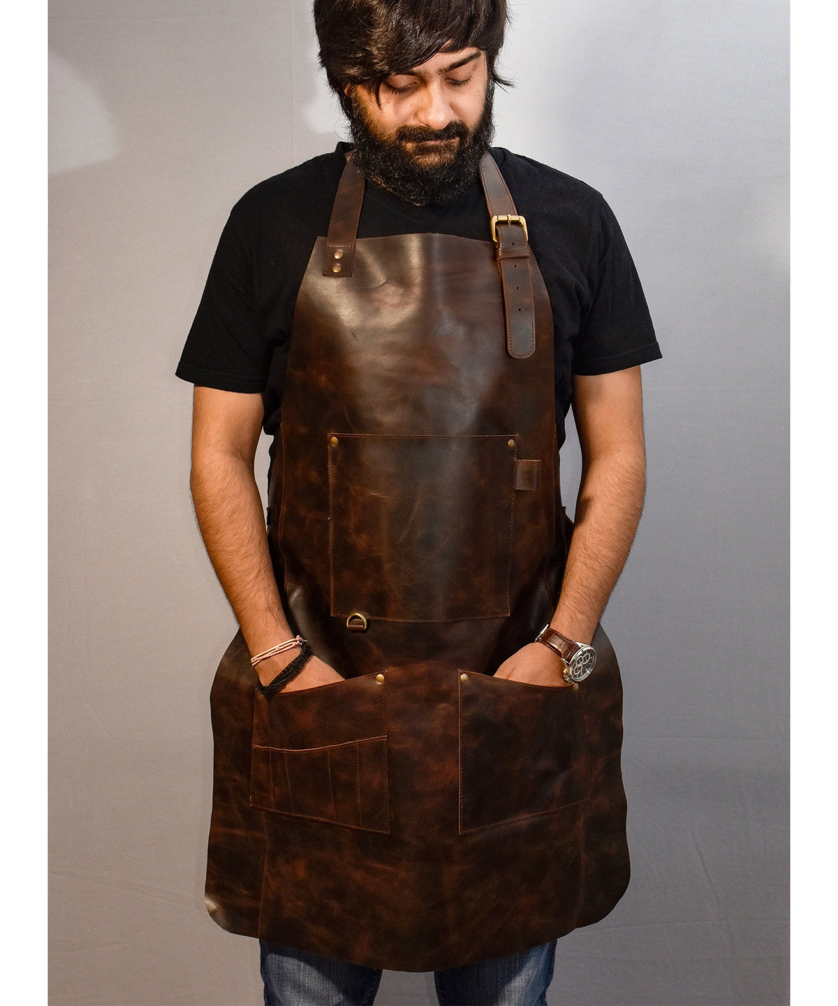 May include: A brown leather apron with multiple pockets and adjustable straps. The apron has a distressed look and is made of thick, durable leather.