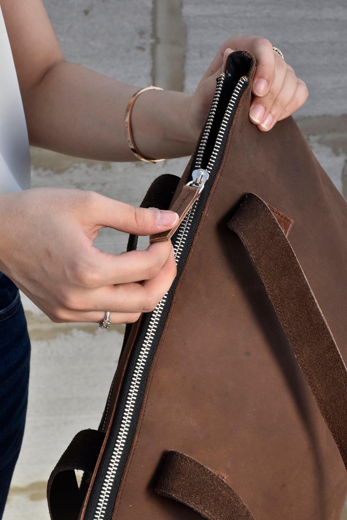 May include: A brown leather tote bag with a zipper closure and a leather strap. The zipper pull is a brown leather tab.