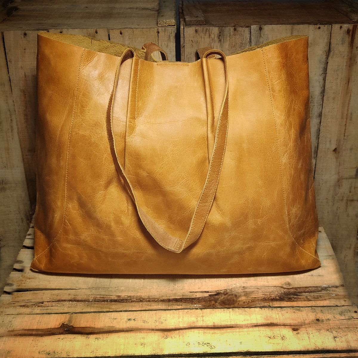 May include: A large, brown leather tote bag with two long straps. The bag is sitting on a wooden surface.