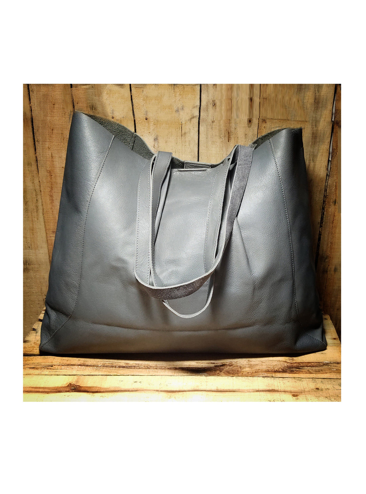 May include: A large gray leather tote bag with two long handles. The bag is sitting on a wooden surface.