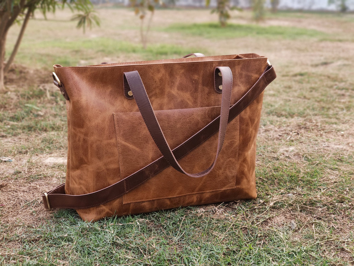 May include: A brown leather tote bag with a long strap and a front pocket. The bag has a distressed look and is made of high-quality leather.