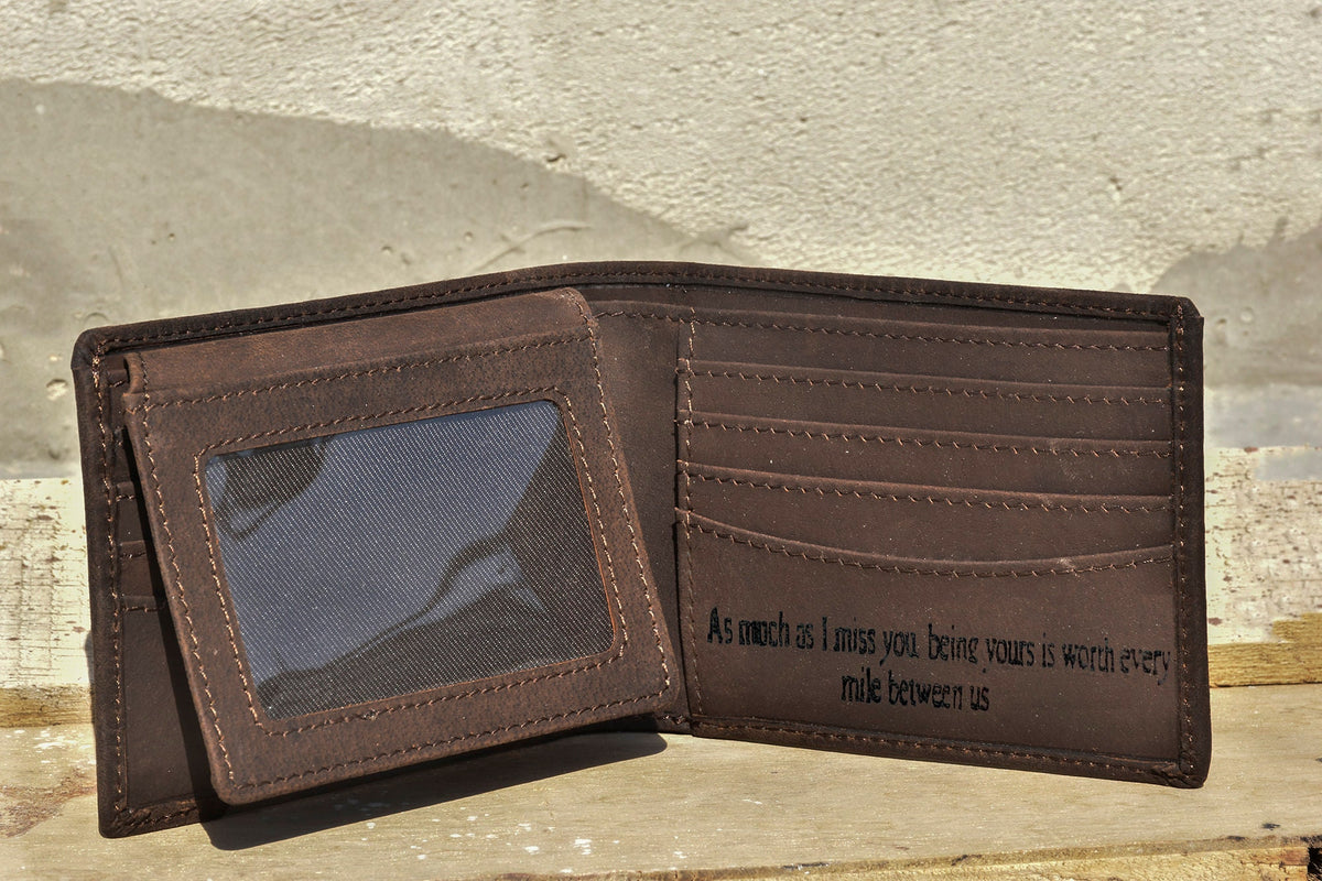 May include: A brown leather wallet with a clear plastic window for a photo ID. The wallet has multiple card slots and a message engraved on the inside: "As much as I miss you being yours is worth every mile between us."