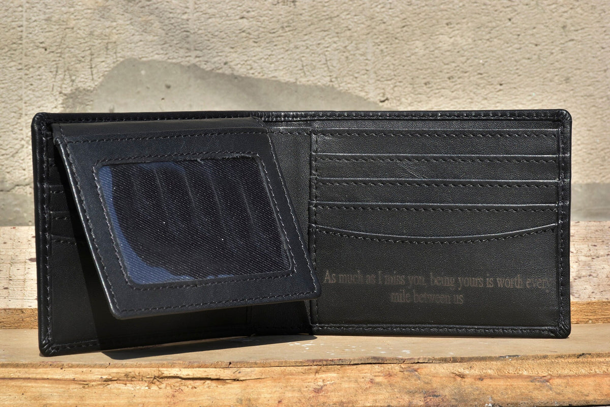 May include: A black leather wallet with a window for a photo ID and multiple card slots. The wallet is open and the inside has an inscription that reads "As much as I miss you, being yours is worth every mile between us."
