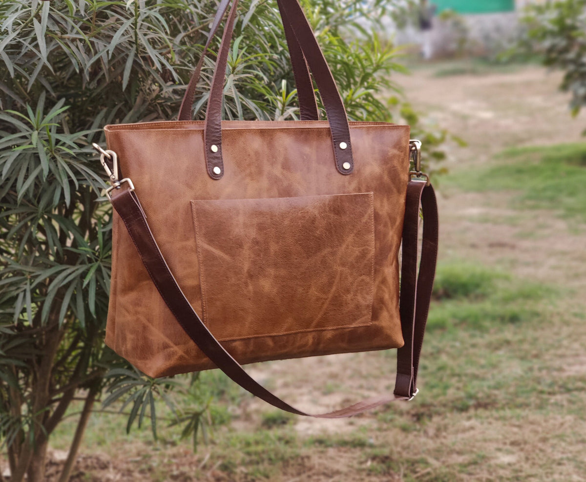 May include: A brown leather tote bag with a front pocket and a detachable shoulder strap. The bag has two top handles and metal hardware. The leather has a distressed look. The bag is designed for everyday use.