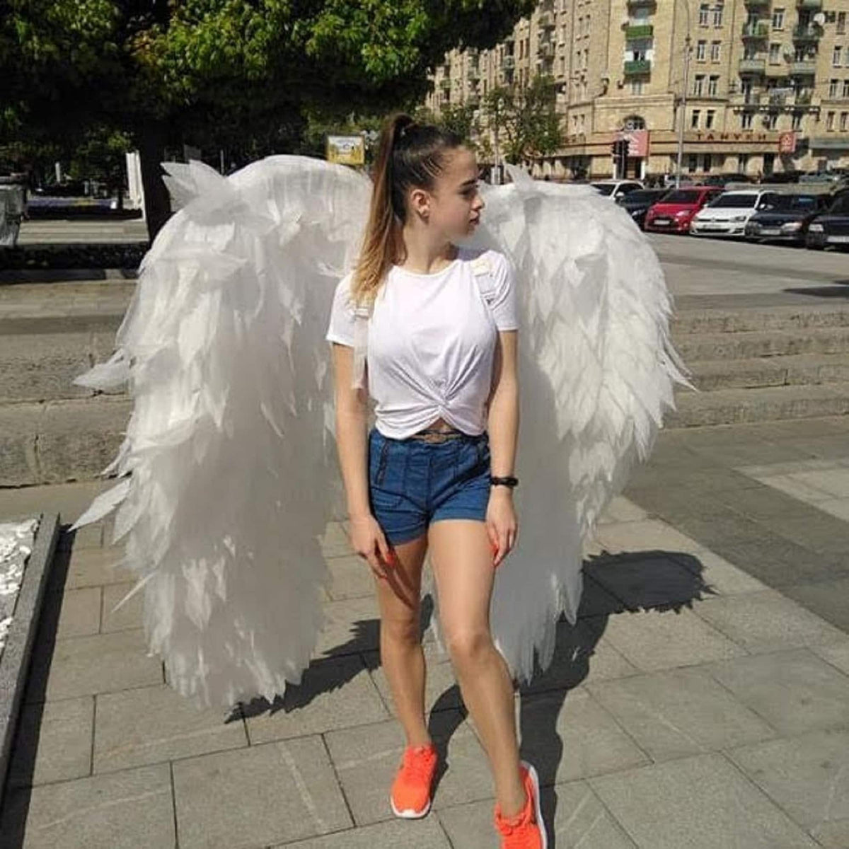 May include: A person wearing a white t-shirt and denim shorts with large white angel wings.