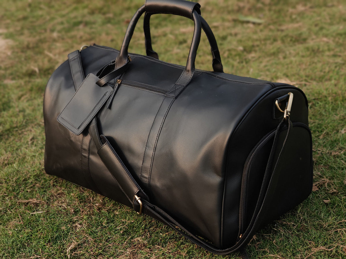 May include: A black leather duffel bag with a gold zipper and a small pocket on the side. The bag has a long strap that can be adjusted to fit comfortably on the shoulder.
