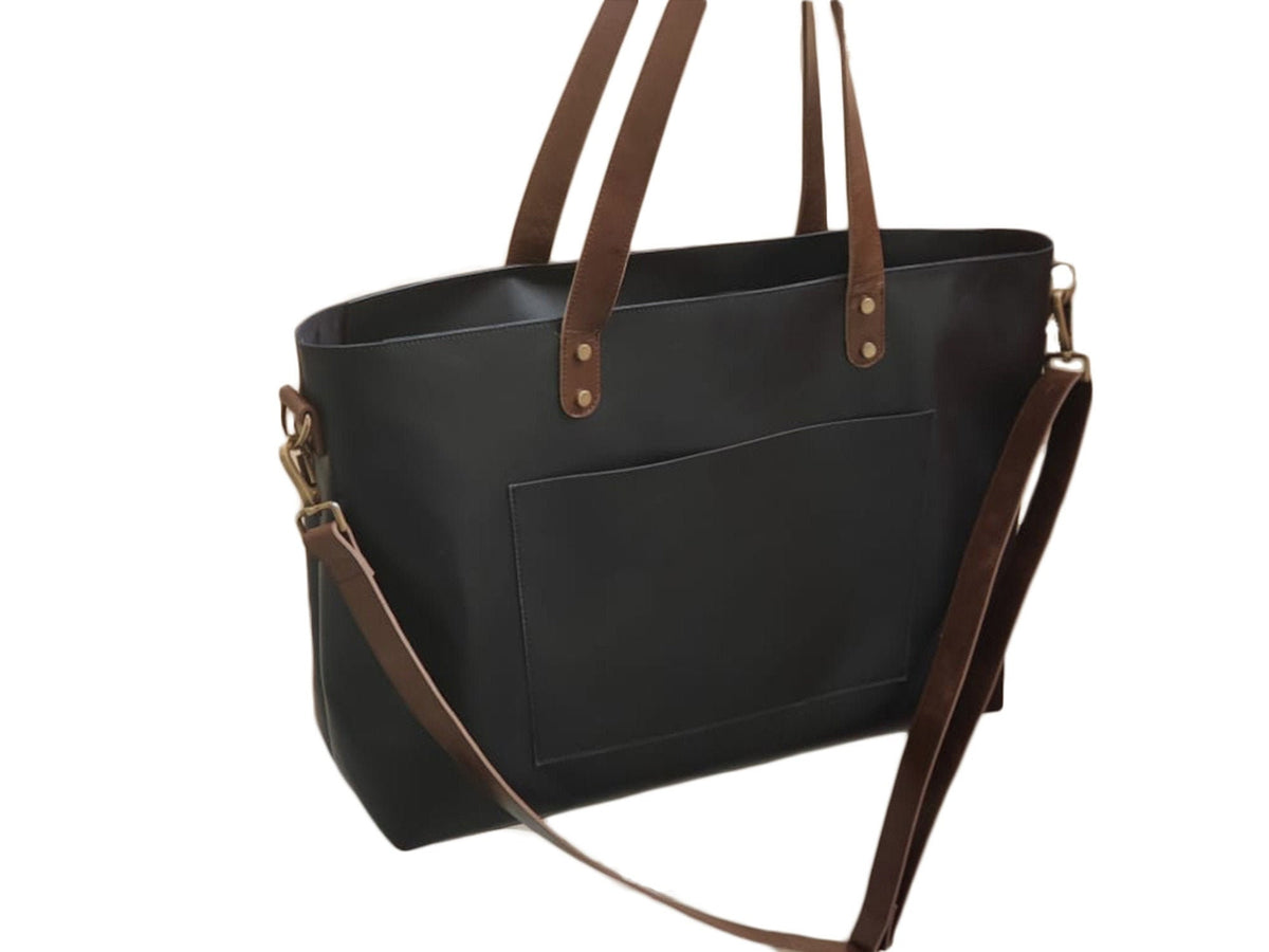 May include: A black leather tote bag with brown leather straps and a front pocket. The bag has a long brown strap that can be used to carry it on the shoulder.