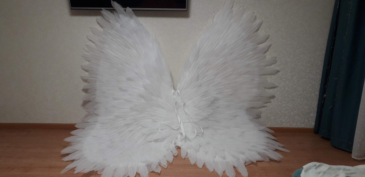 May include: A pair of large, white angel wings made of feathers. The wings are spread out and are lying on a wooden floor.