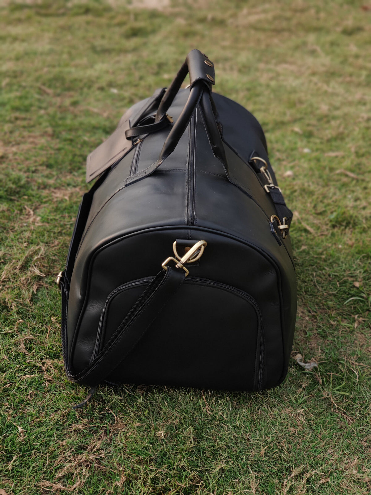 May include: Black leather duffel bag with a top handle and a shoulder strap. The bag has gold-colored hardware and a zipper closure.