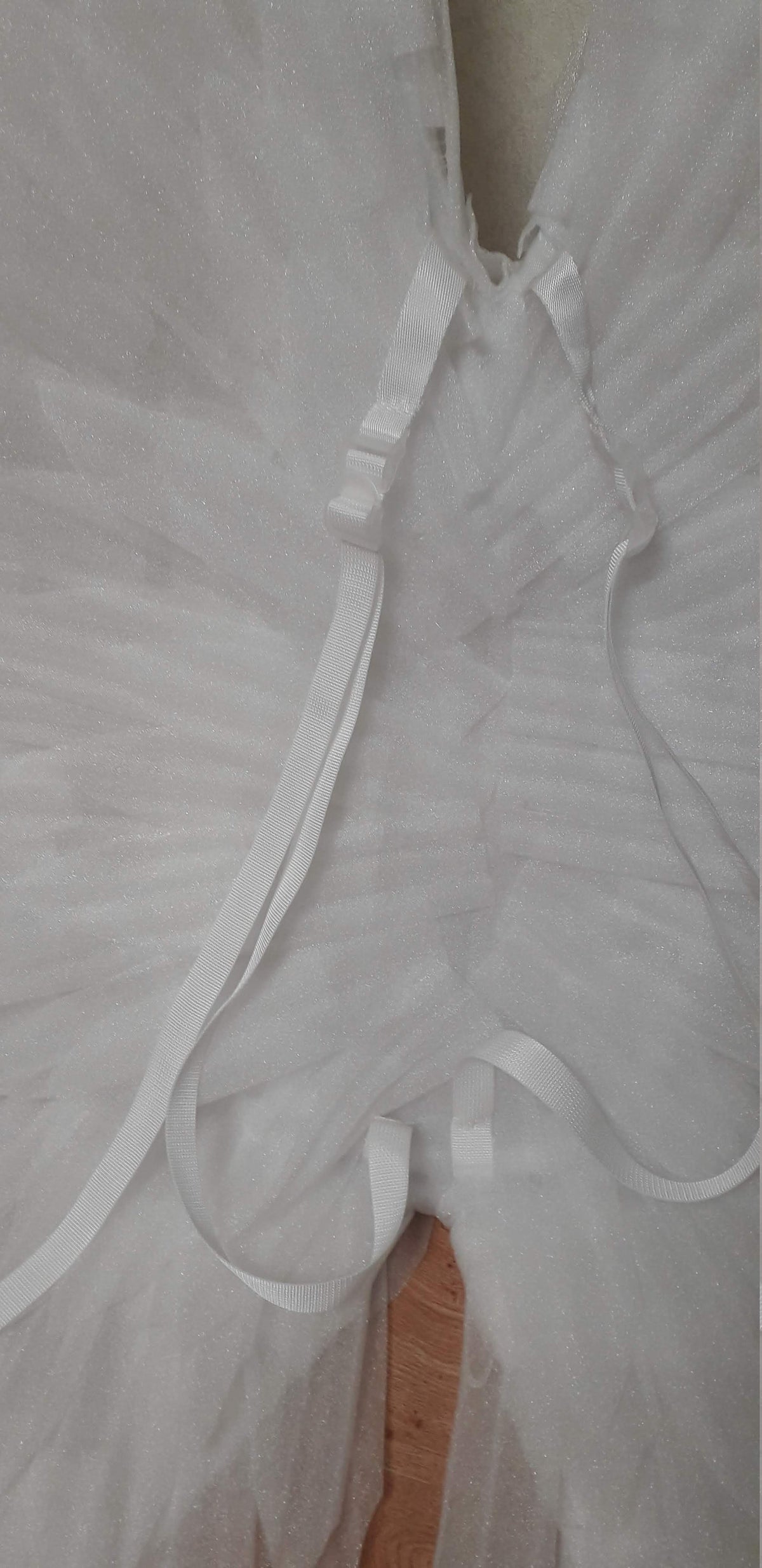 May include: White tulle angel wings with white straps and a buckle closure. The wings are made of a soft, sparkly material.