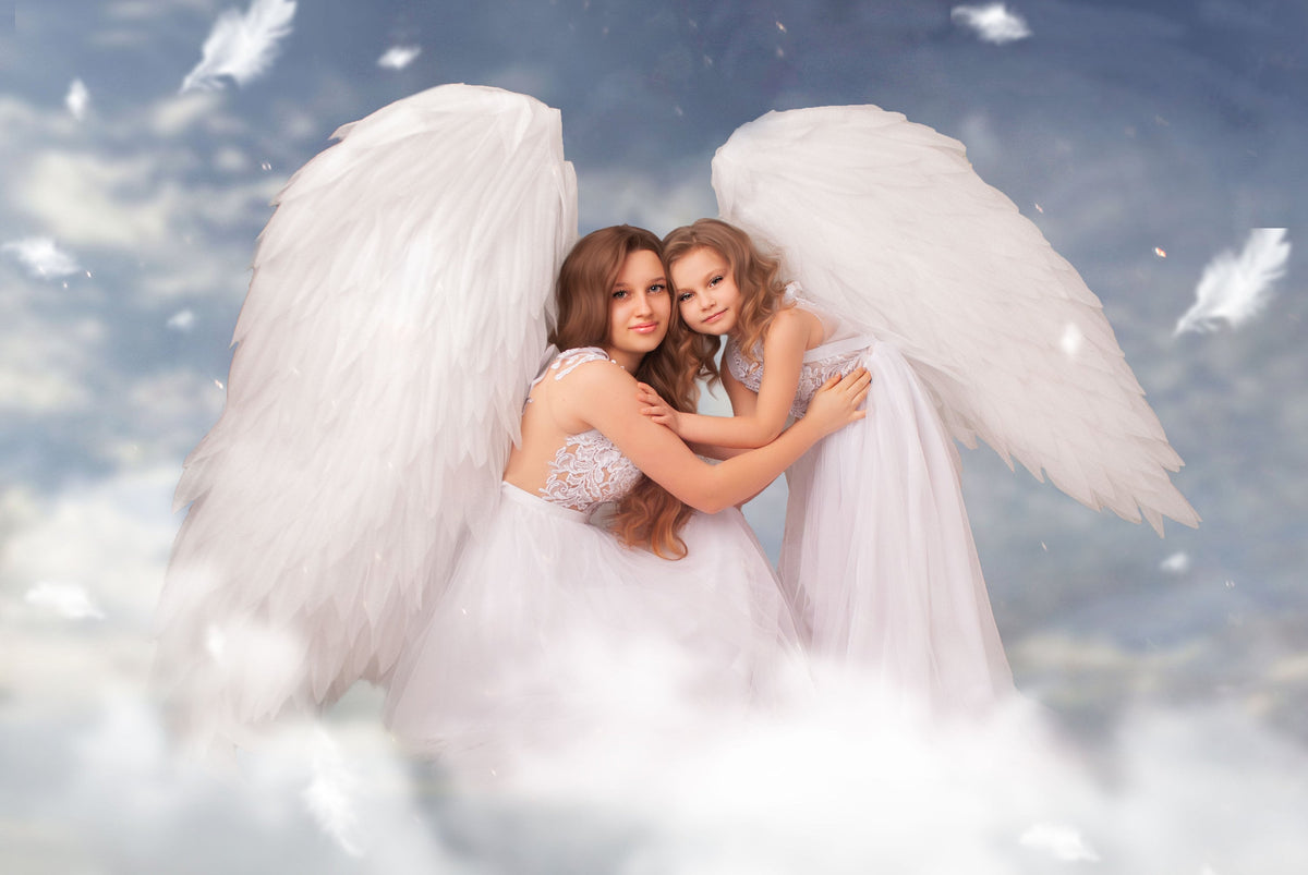 May include: Two individuals wearing white dresses and large white feathered wings, posing against a cloudy sky background. One is embracing the other. The image evokes a heavenly or angelic theme.