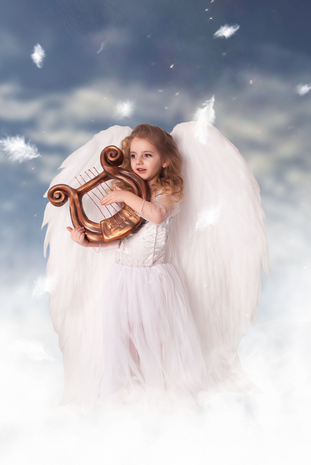 May include: A young girl dressed as an angel with large white wings plays a golden lyre. She is standing in a cloud-like setting with a blue sky in the background.