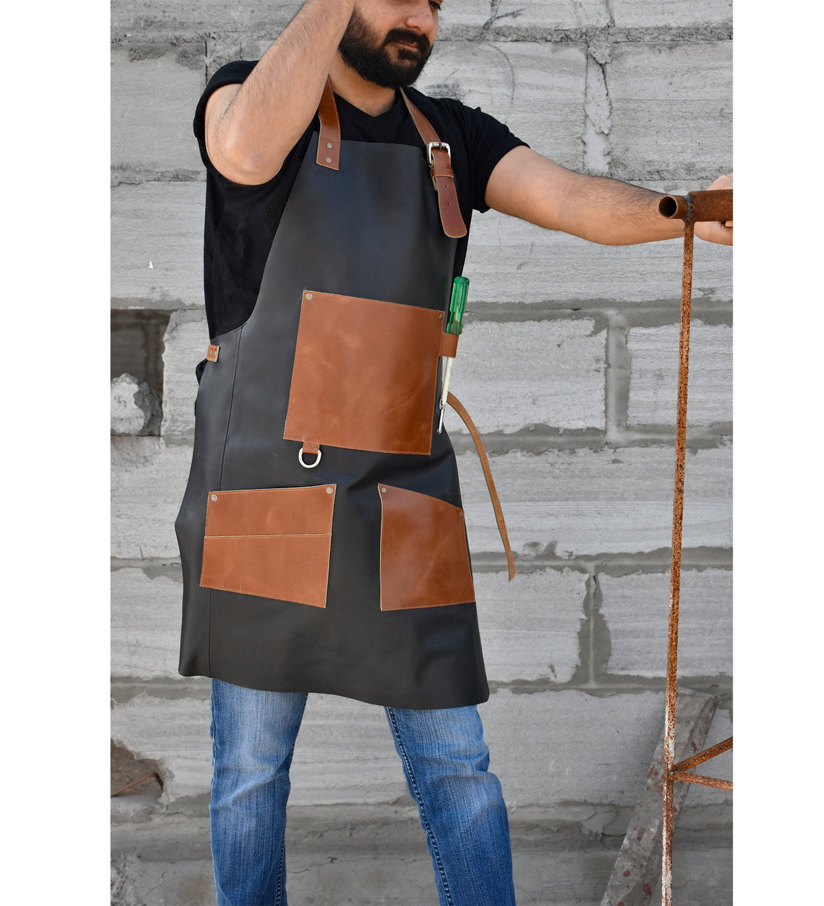 May include: A black leather apron with brown leather pockets and a tool loop. The apron has adjustable straps and a metal ring on the front.