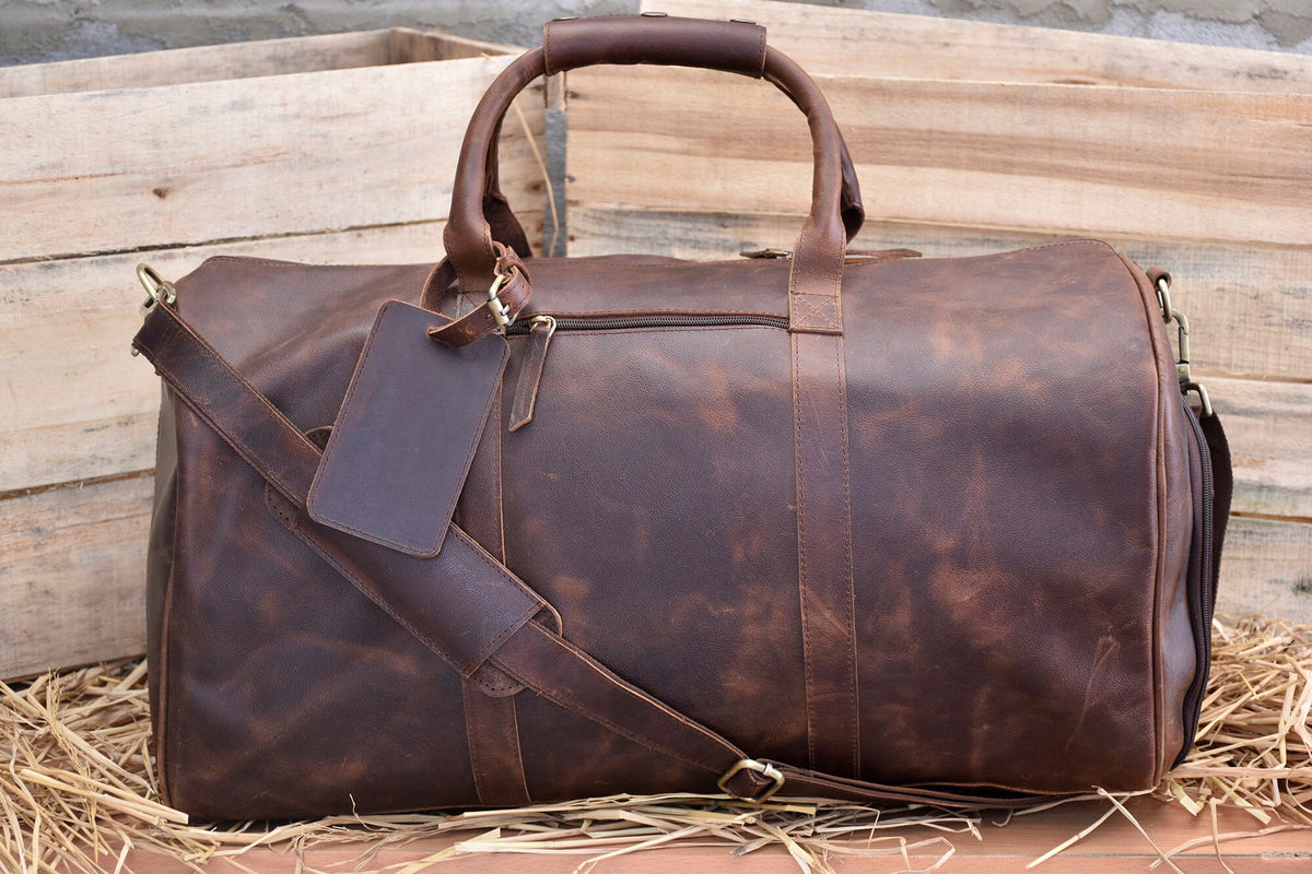 May include: A brown leather duffel bag with a shoulder strap and a luggage tag. The bag has a distressed look and is made of high-quality leather.