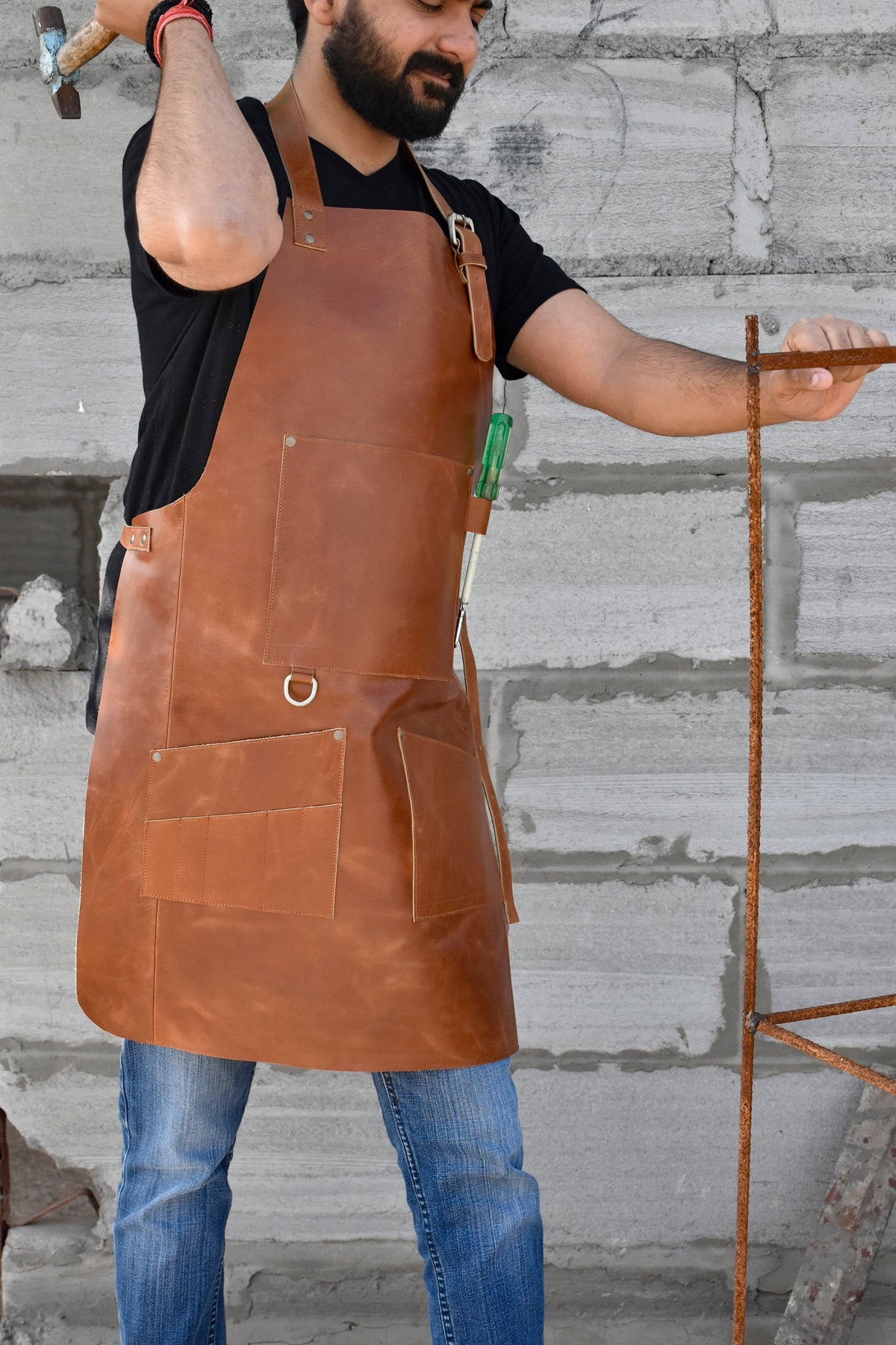 May include: A brown leather apron with multiple pockets and a tool loop. The apron is worn by a person standing in front of a brick wall.