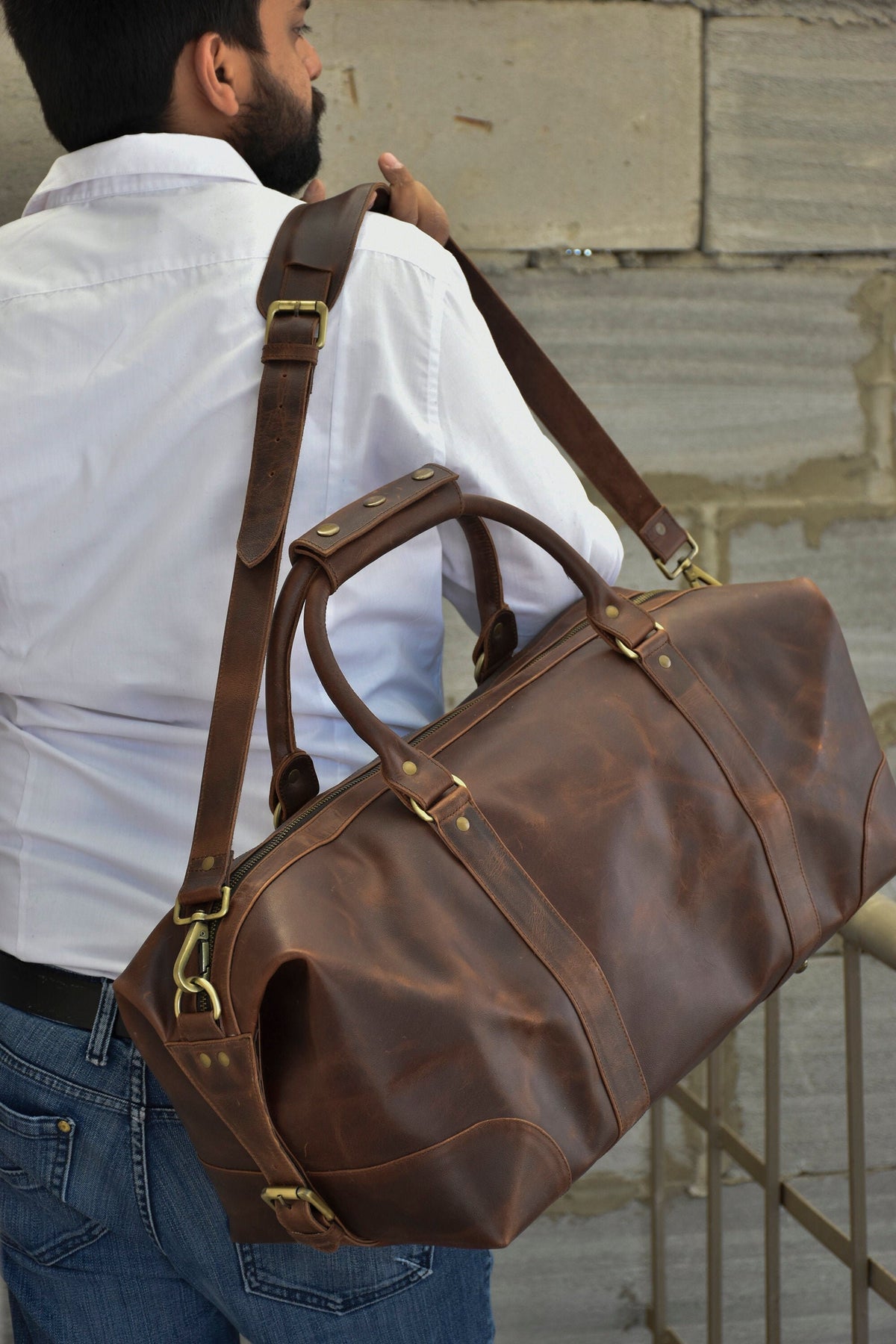 May include: A brown leather duffel bag with brass hardware and a long adjustable shoulder strap. The bag has a top handle and a zipper closure.