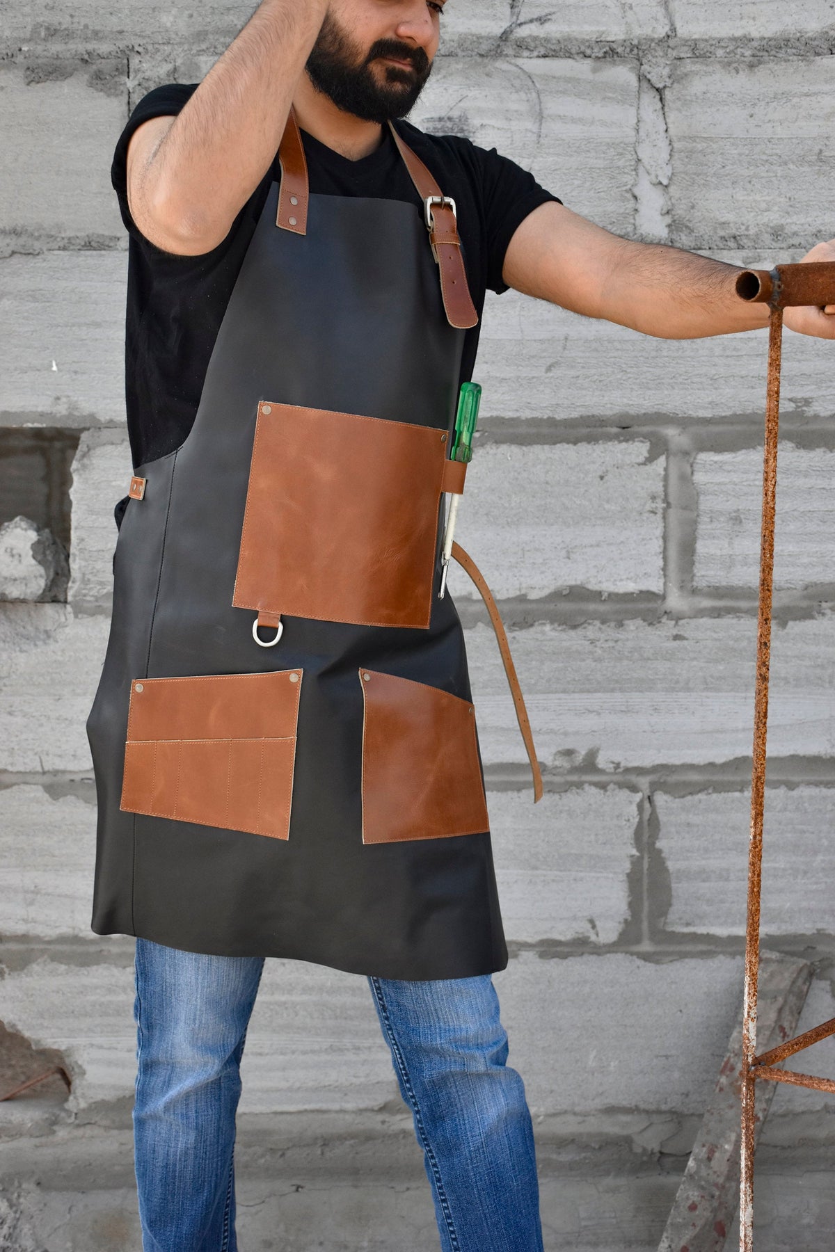 May include: A black leather apron with brown leather pockets and a tool loop. The apron has a strap that goes around the waist and a buckle.