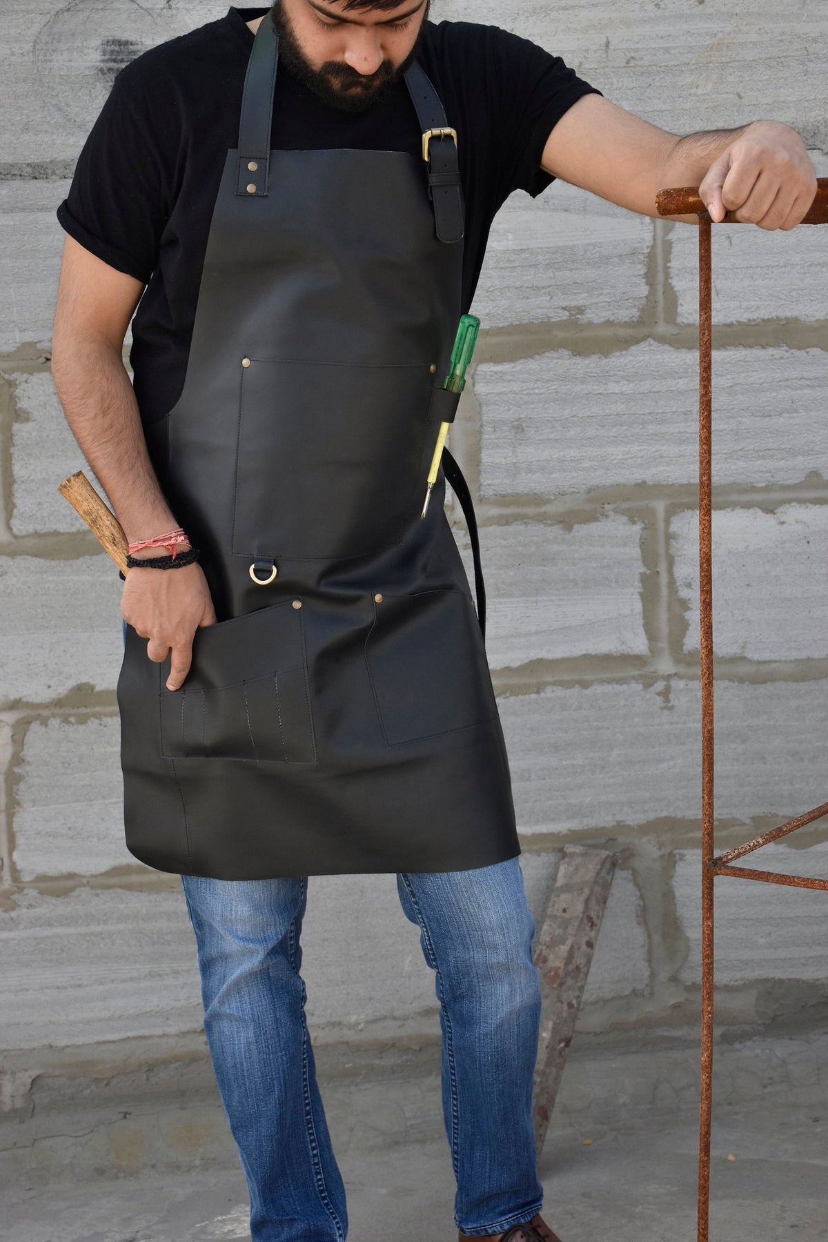 May include: A black leather apron with a large pocket and a tool holder. The apron has adjustable straps and a metal buckle.