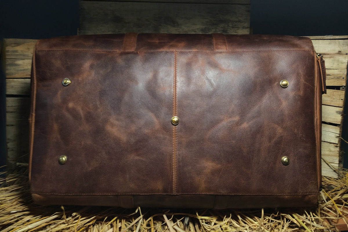 May include: A brown leather duffel bag with brass accents. The bag has a textured surface and a zipper closure.