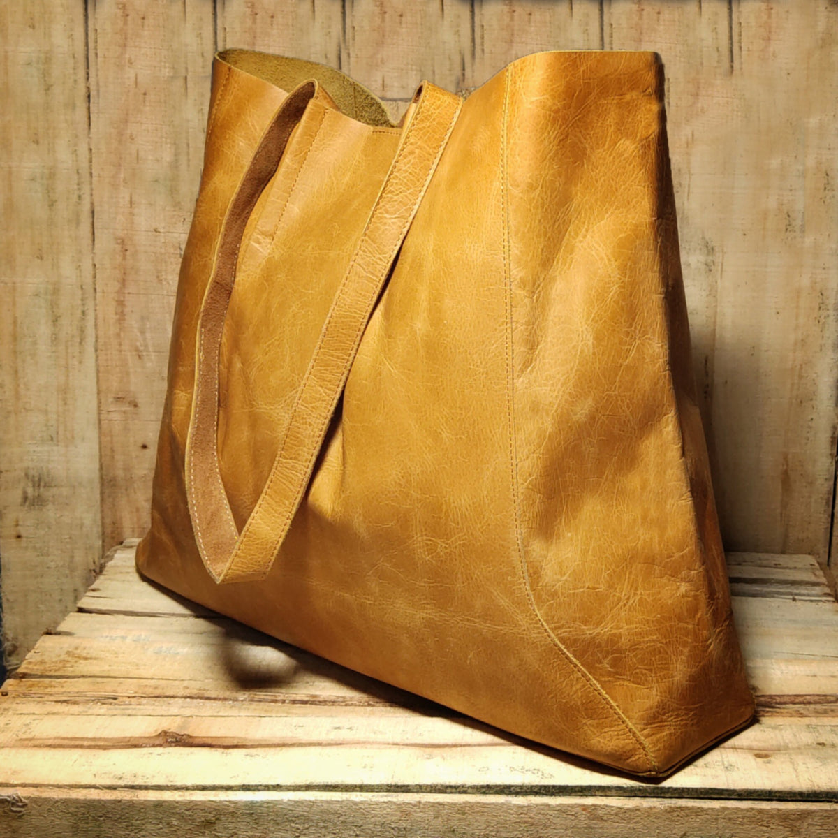 May include: A large, tan leather tote bag with two long straps. The bag has a slightly distressed look and is made of a soft, supple leather.