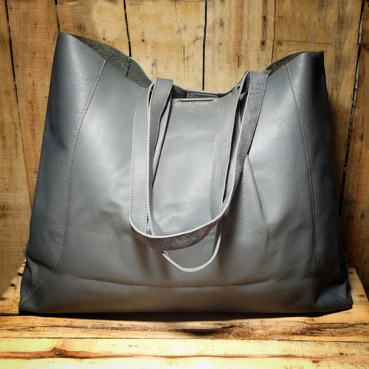 May include: A large gray leather tote bag with two long straps. The bag is made of a soft, supple leather and has a spacious interior.