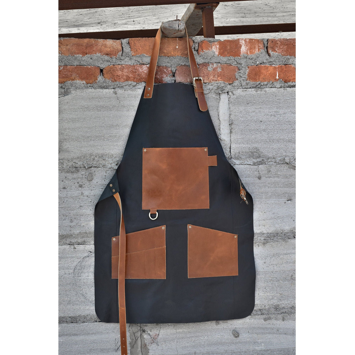 May include: A black canvas apron with brown leather accents and pockets. The apron has a large pocket on the front and two smaller pockets on the sides.