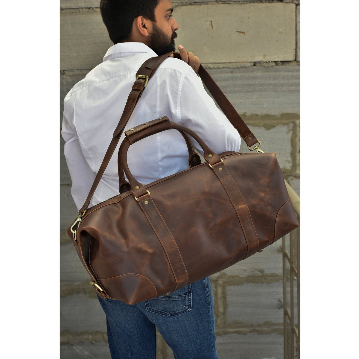 May include: A brown leather duffel bag with brass hardware and a long adjustable shoulder strap. The bag has a top handle and a spacious main compartment.