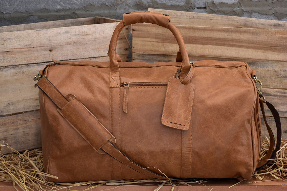 May include: A large, brown leather duffel bag with a top handle and a detachable shoulder strap. The bag features a luggage tag and a zippered closure. The bag is made of a distressed leather material.