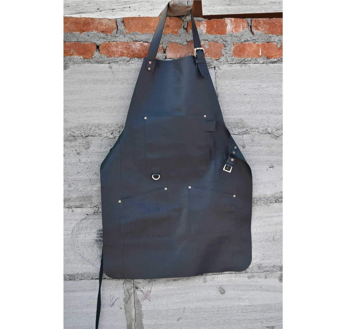 May include: A black leather apron with multiple pockets and a metal ring. The apron has adjustable straps and a buckle closure.