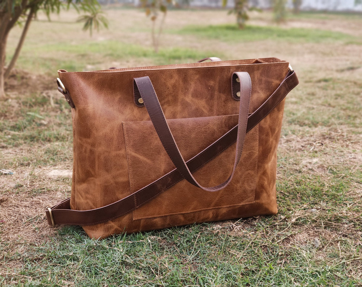 May include: A brown leather tote bag with a long strap and two shorter handles. The bag has a front pocket and a distressed look.