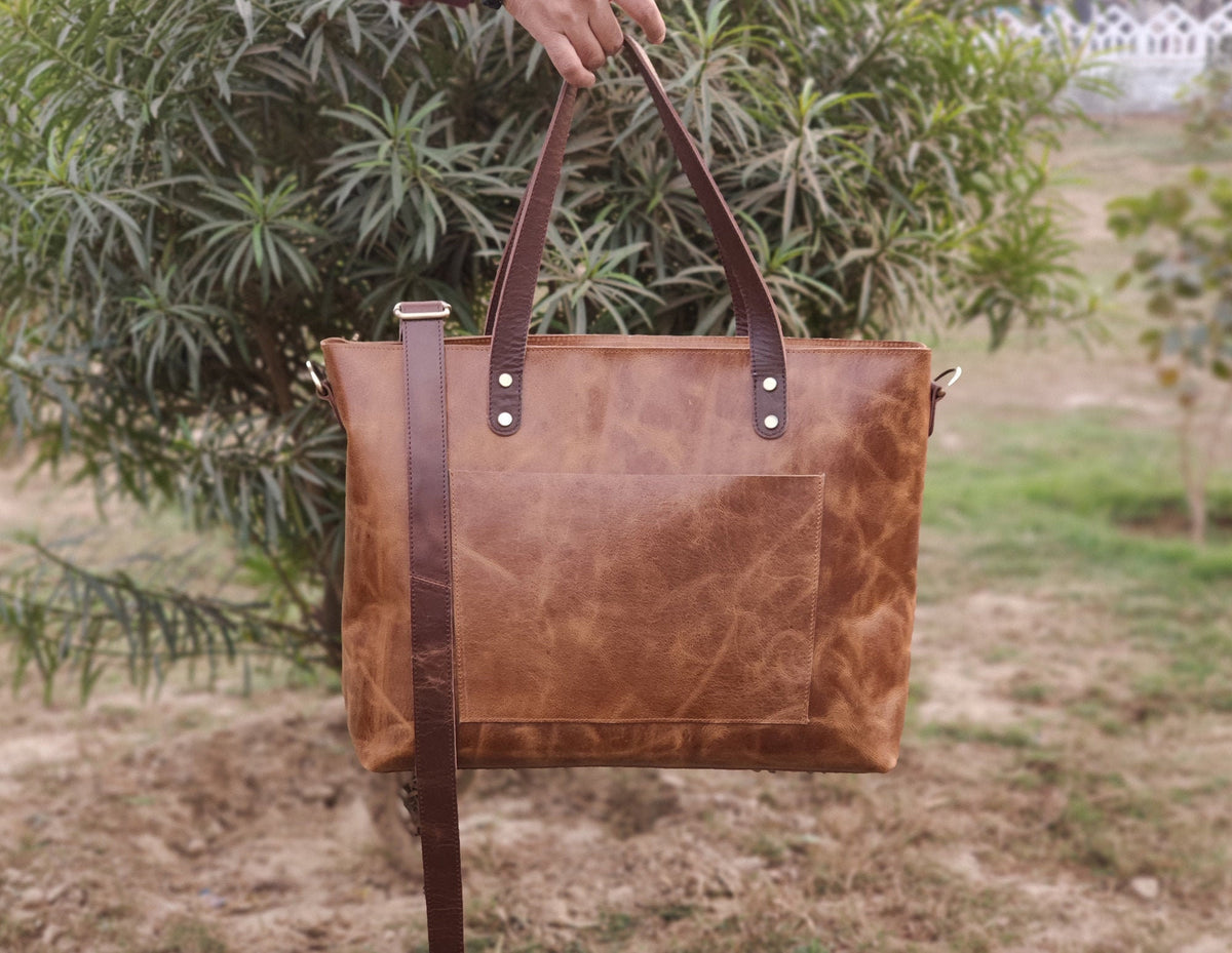 May include: A brown leather tote bag with a long strap. The bag has a pocket on the front and two silver rivets on the top.