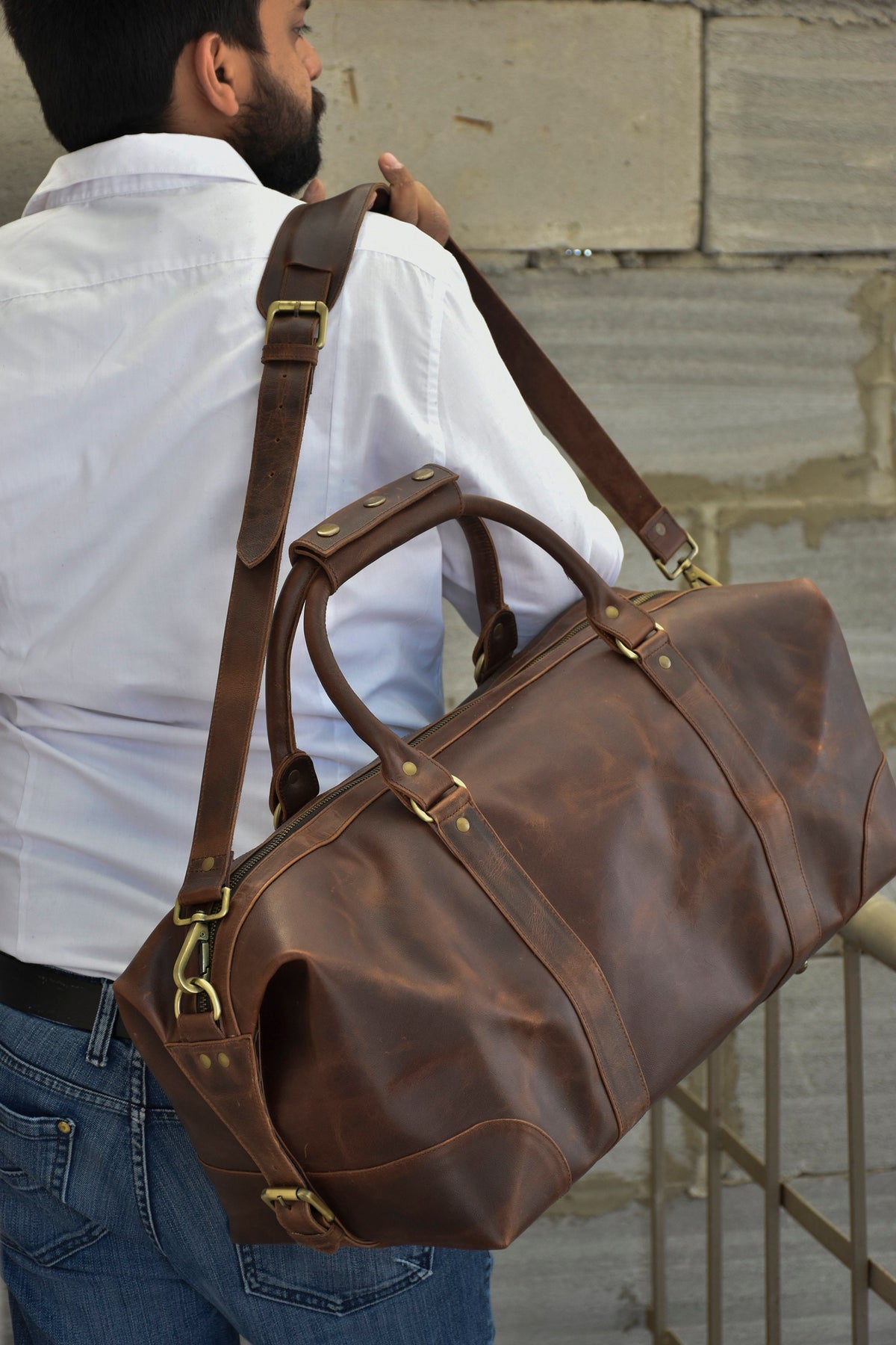 May include: A brown leather duffel bag with a long strap and brass hardware. The bag has a zipper closure and two top handles.