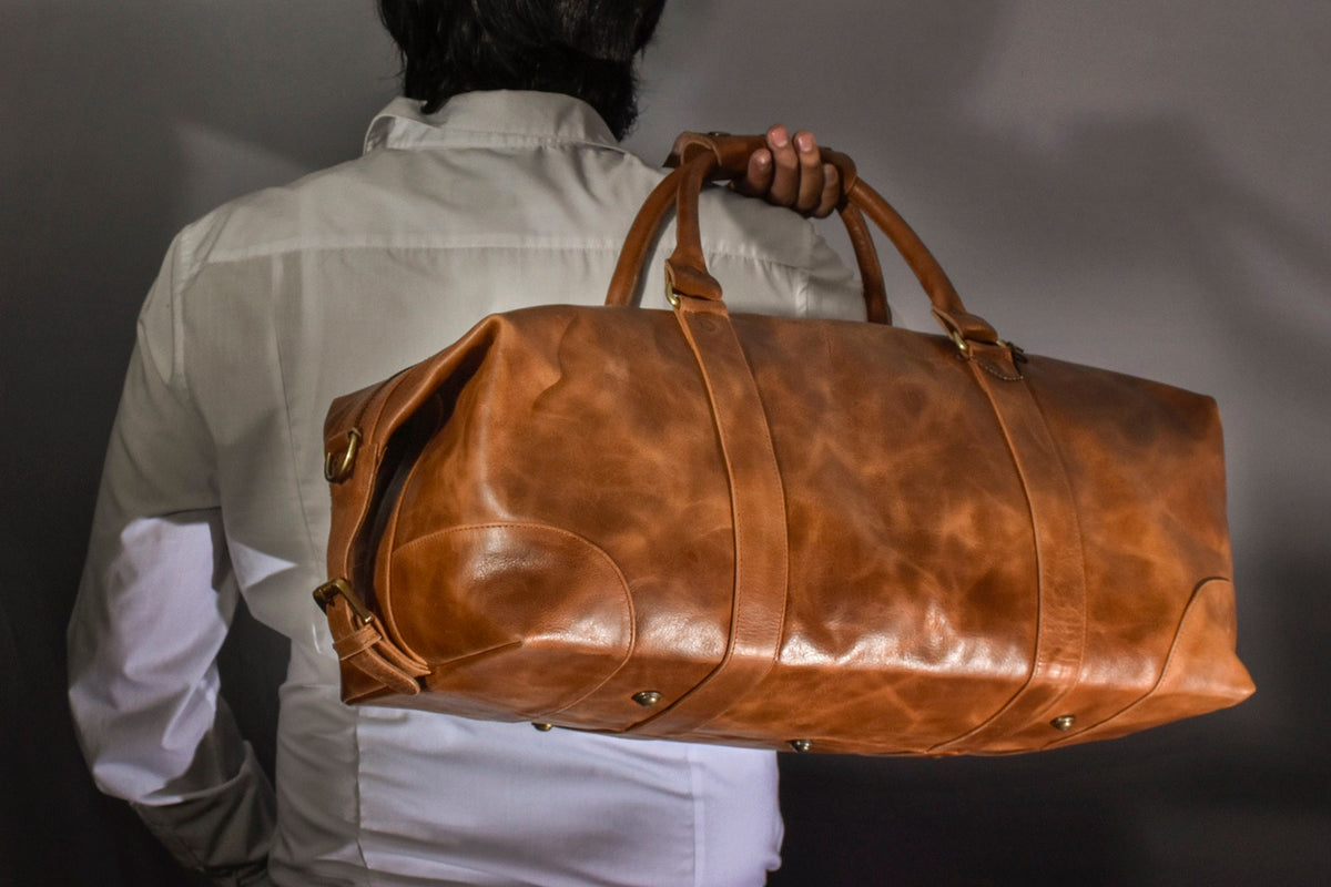 May include: A brown leather duffel bag with brass hardware. The bag has a top handle and a shoulder strap.