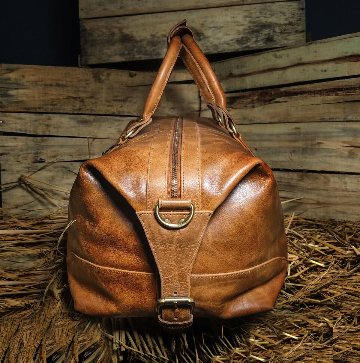 May include: A brown leather duffel bag with a zipper closure and a buckle strap. The bag has two top handles and a brass D-ring on the front.