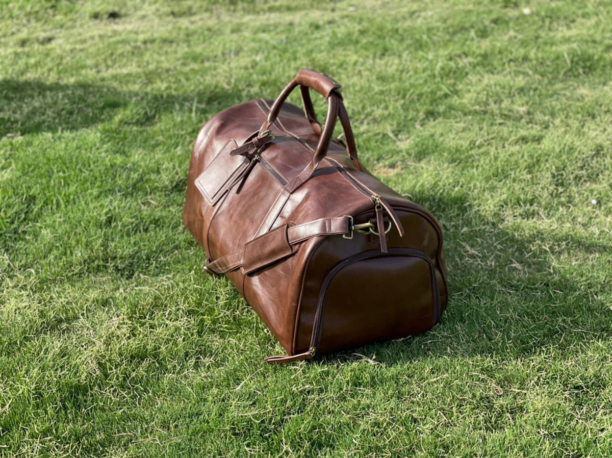 May include: A brown leather duffel bag with a top handle and a shoulder strap. The bag has a zipper closure and a front pocket.