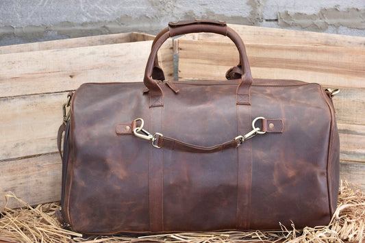 May include: A brown leather duffel bag with a top handle and a shoulder strap. The bag has a zipper closure and metal hardware.
