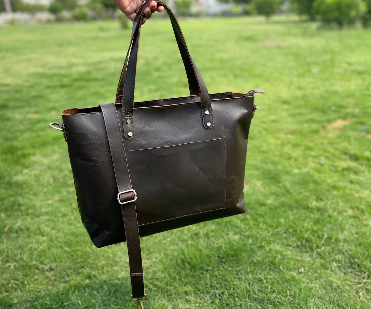May include: A brown leather tote bag with a long shoulder strap and two top handles. The bag has a front pocket and a zipper closure.
