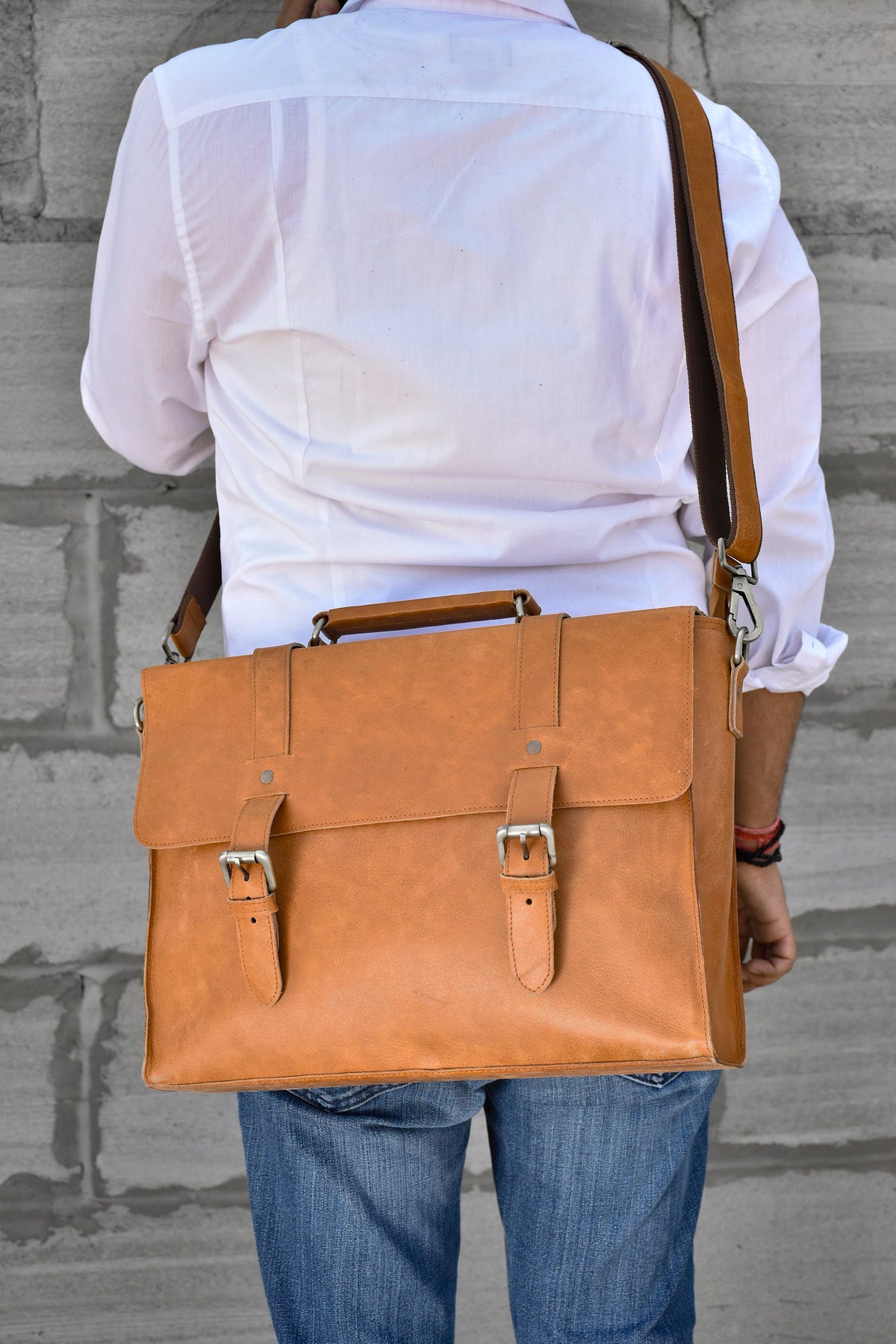 May include: A brown leather messenger bag with a long adjustable strap. The bag has two buckles on the front and a flap closure.