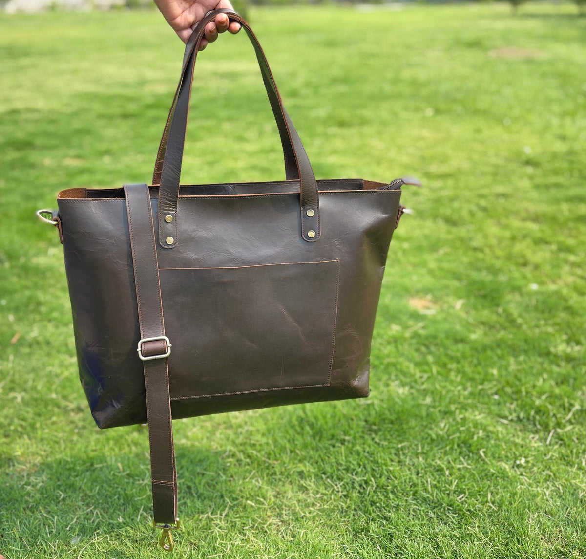 May include: A brown leather tote bag with a long shoulder strap and two top handles. The bag has a front pocket and a zipper closure.