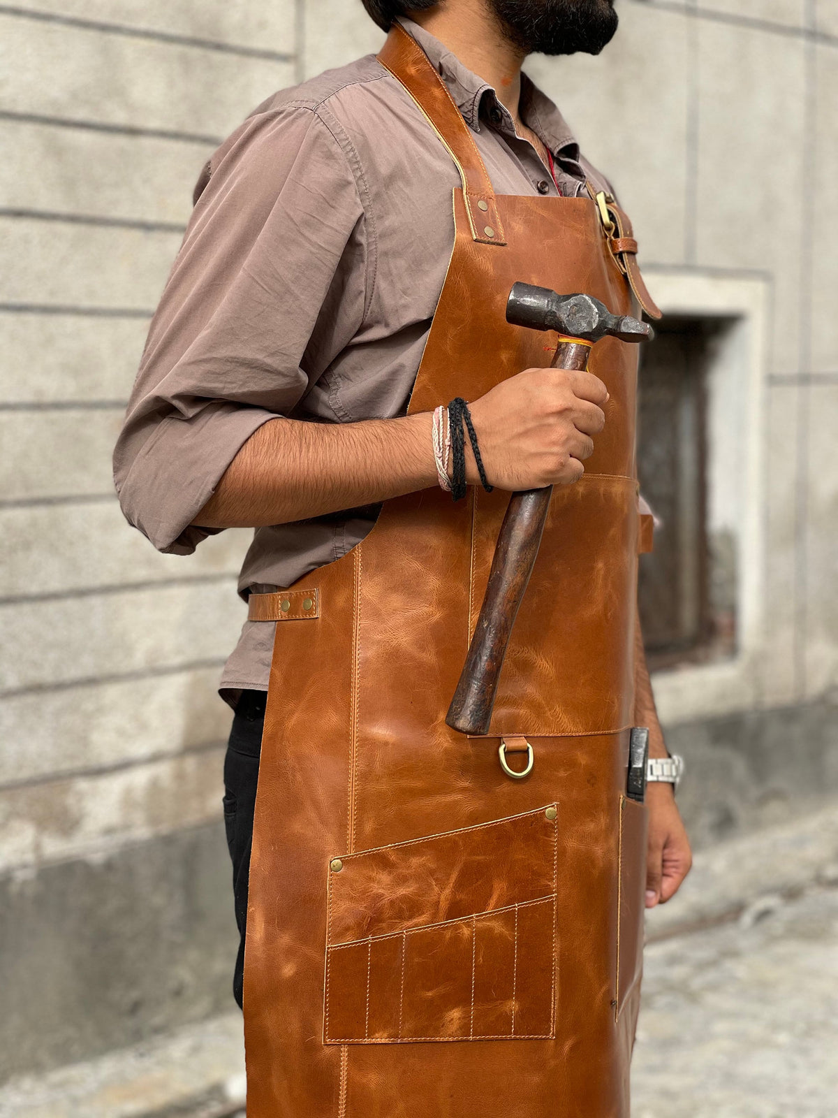 May include: A brown leather apron with multiple pockets and a hammer tucked into the side pocket.