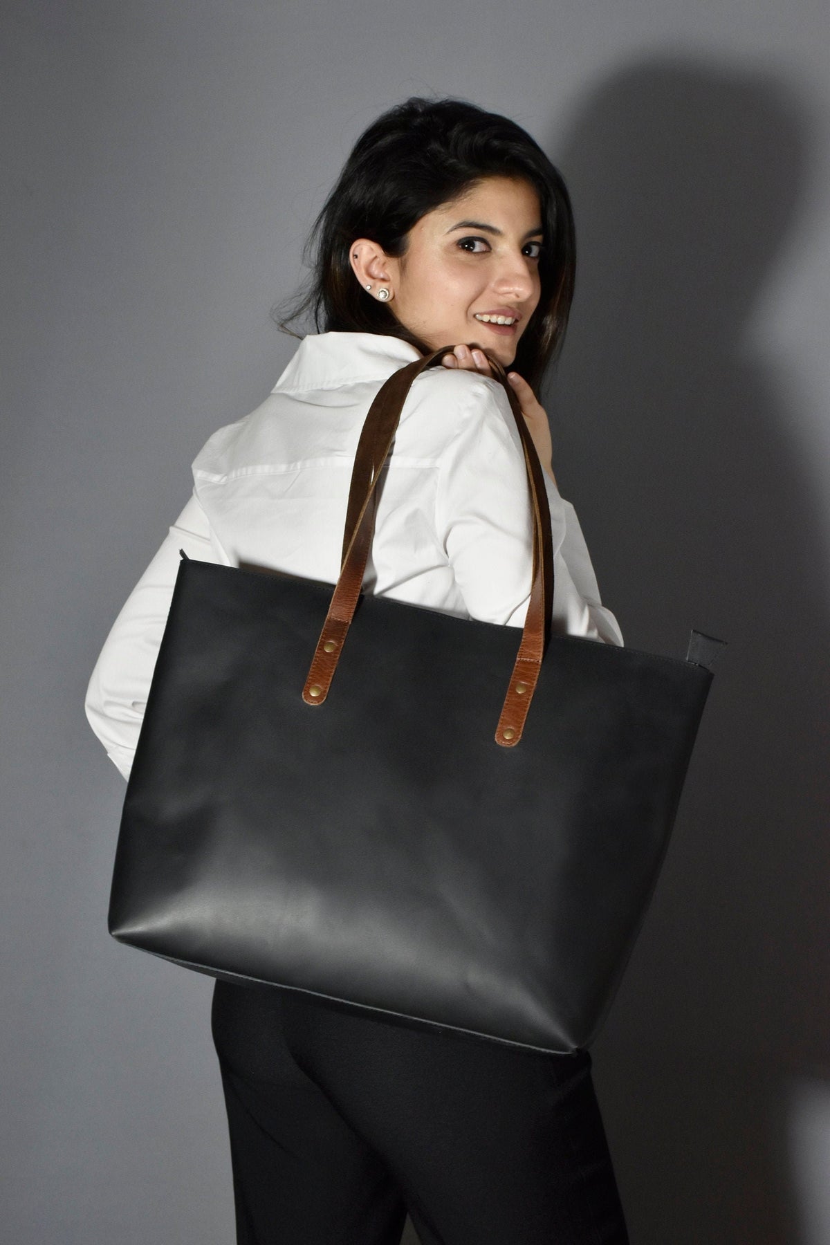 May include: A black leather tote bag with brown leather straps and gold accents. The bag has a spacious interior and is perfect for carrying everyday essentials.