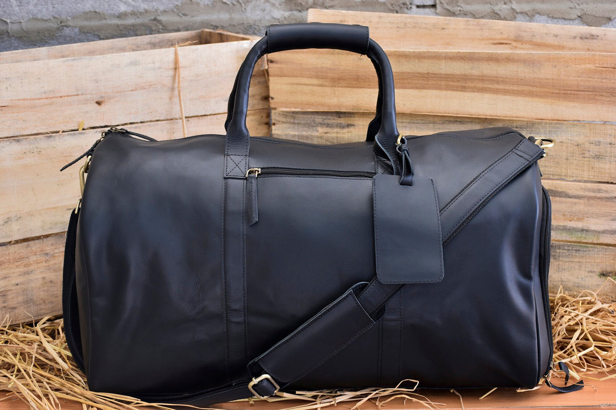 May include: A black leather duffel bag with a top handle and a shoulder strap. The bag has a zipper closure and a small leather tag attached to the front.