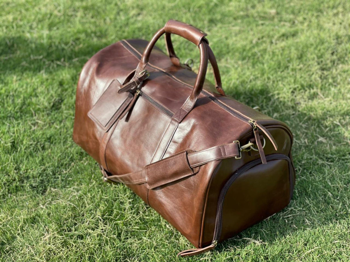 May include: A brown leather duffel bag with a top handle and a shoulder strap. The bag has a zipper closure and a small pocket on the front.