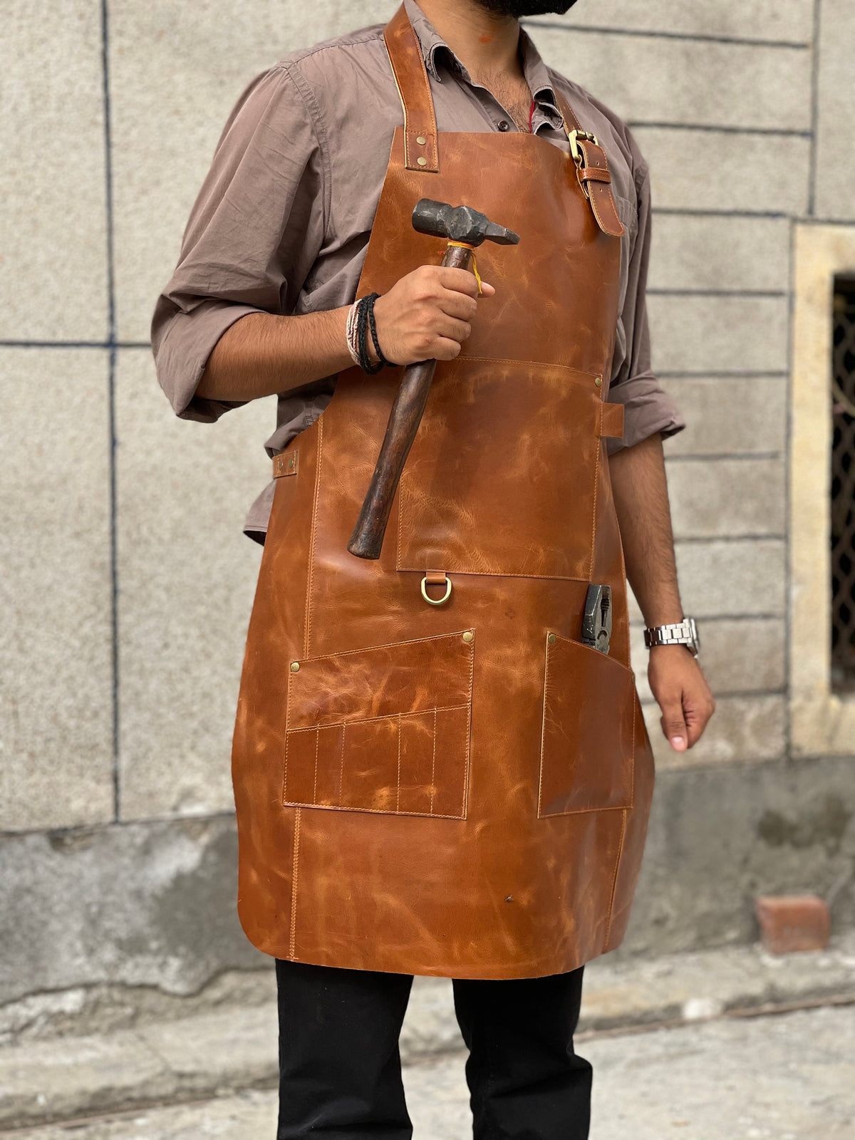 May include: A brown leather apron with multiple pockets and a hammer. The apron has a brass buckle and a D-ring.