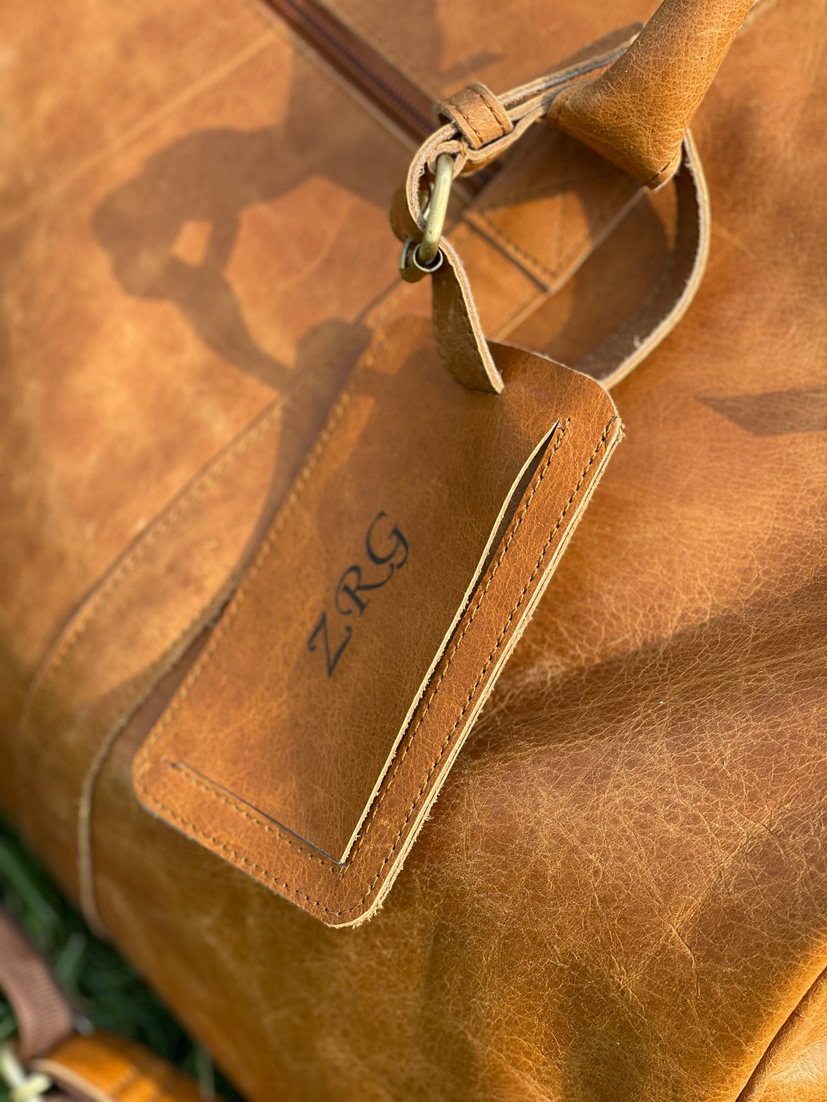 May include: A brown leather travel bag with a leather luggage tag that says "ZRG" in black lettering.